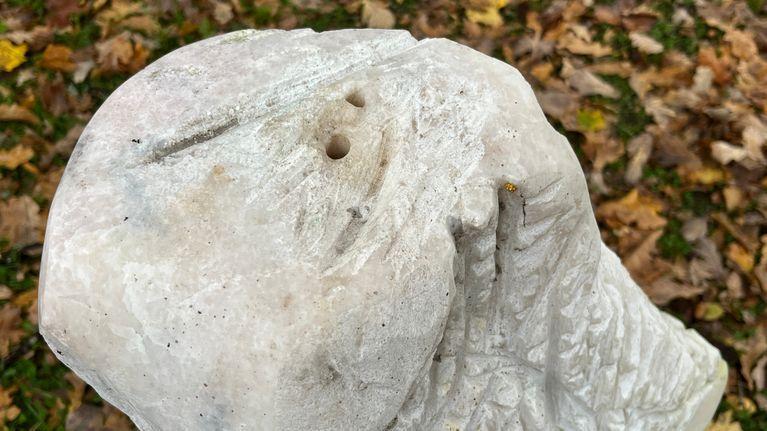 None Statua scolpita in pietra chiara, con due fori nella parte superiore, sullo sfondo foglie autunnali a terra.