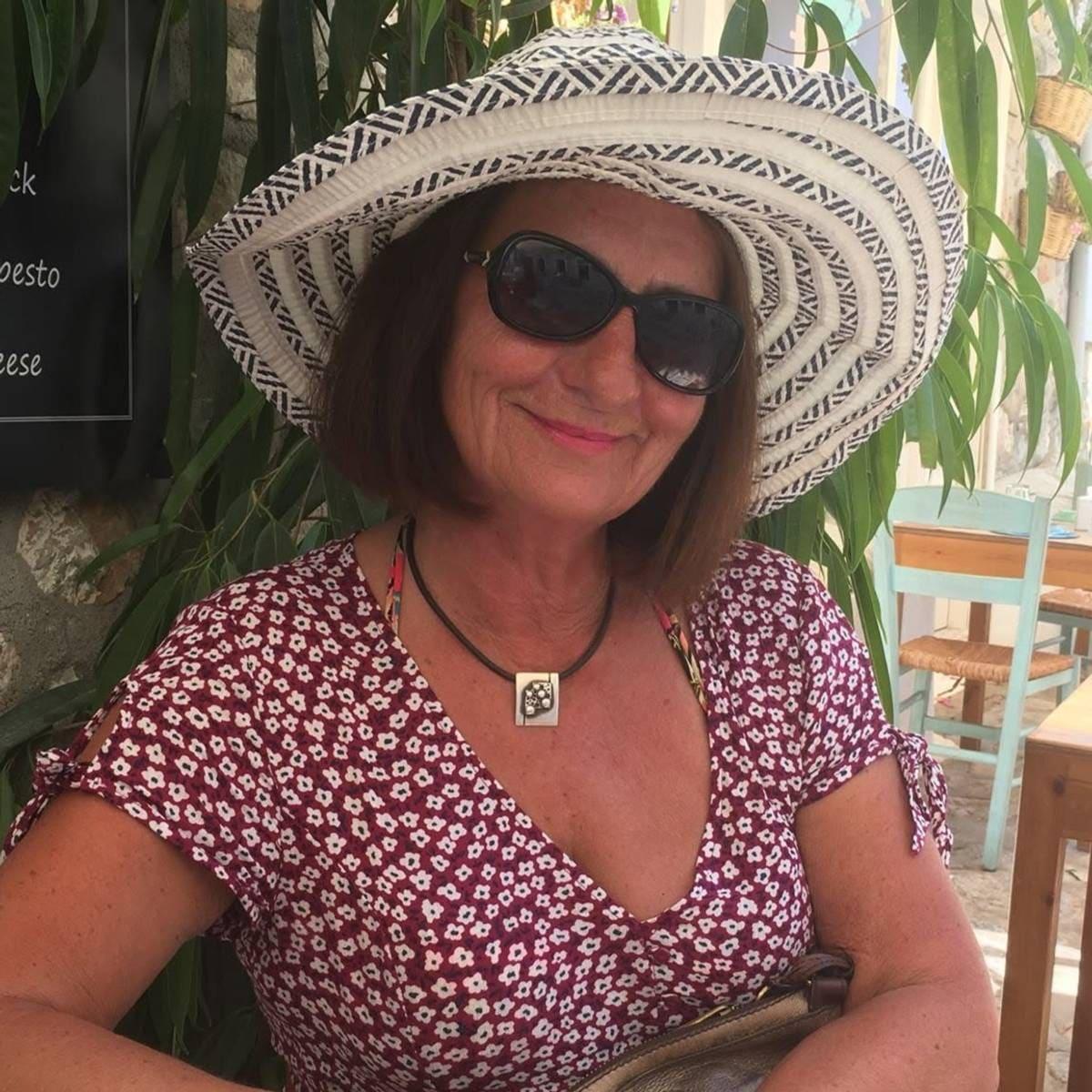 Foto: Privat Una donna con cappello da sole e occhiali da sole sorride a un tavolo di un ristorante all’aperto. (Descrizione dell’immagine generata da un servizio di IA)