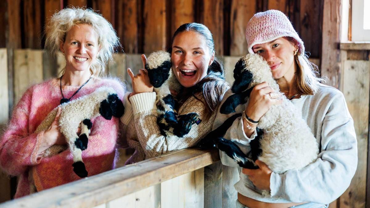Foto: Martin Litwicki / SYFTESTAD GARD AS Tre donne tengono ciascuna un agnellino all’interno di una stalla con pareti di legno. (Descrizione dell’immagine generata da un servizio di IA)