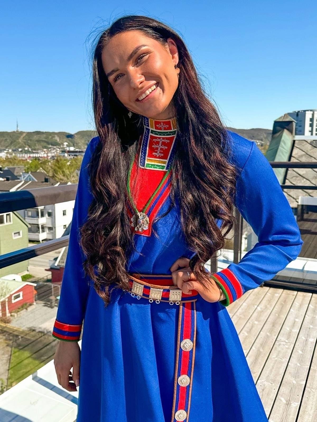 Foto: Privat Una donna con lunghi capelli scuri è in piedi su una terrazza, vestita con un gákti blu. Sullo sfondo si vede una città. (Descrizione dell’immagine generata da un servizio di IA)