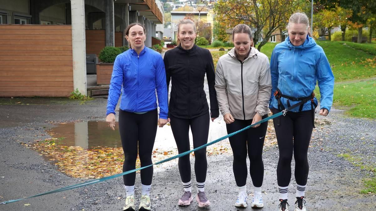 Quattro donne sono in fila, pronte a fare jogging. Indossano giacca e leggings e il terreno è bagnato.