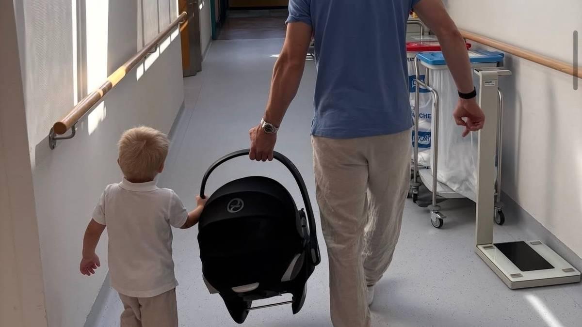 Foto: Privat Un uomo e un bambino camminano lungo il corridoio di un ospedale. L’uomo porta un seggiolino auto per neonati. (La descrizione dell’immagine è stata generata da un servizio di IA)