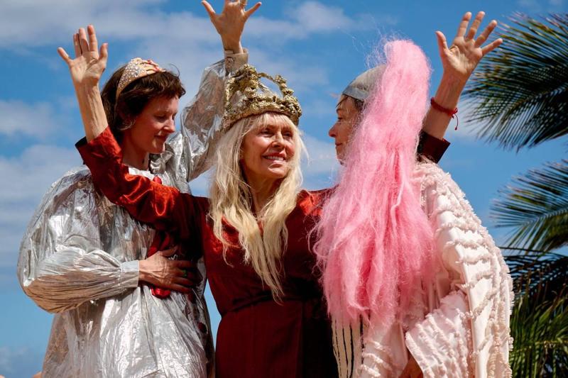 Foto: Rog Baker Ashton / Mer Film Tre donne in costumi colorati tengono le mani alzate.