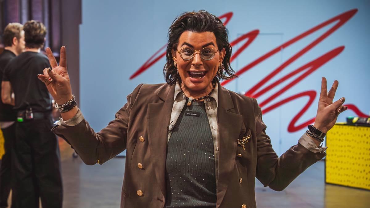 Foto: Kristoffer Steffensen Lenes / TV2 Una persona con gli occhiali e una giacca marrone fa il segno della vittoria con entrambe le mani in uno studio. (Descrizione dell’immagine generata da un servizio di IA)
